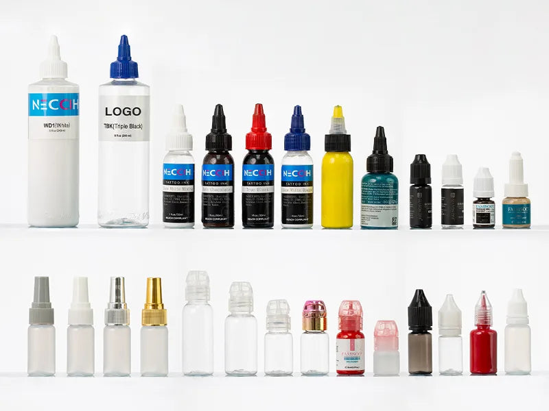 Two rows of small tattoo bottles and dropper bottles arranged on a white background, including clear bottles, black and white bottles, yellow, blue, and red bottles, with some bottles labeled 'NECCIH' and 'LOGO'.