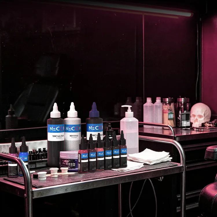A tattoo ink kit with multiple bottles of NECCIH Ink products arranged on a metal cart in a dimly lit studio environment.